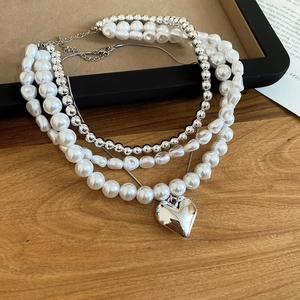 Détail d'un collier de perles multicouches avec pendentif coeur argenté et chaîne