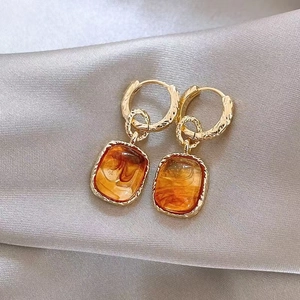 Detail of gold geometric earrings with amber resin on smooth grey silk background