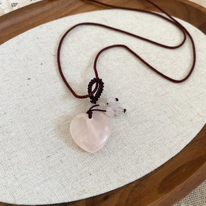 Macro shot of heart-shaped rose quartz pendant on woven brown cord necklace