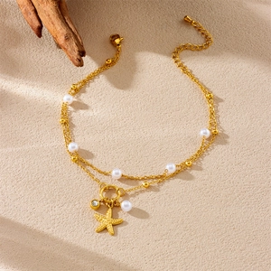 Double-layered gold starfish anklet with pearls and zircon pendant on a textured surface