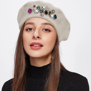 Detail of wool beret with colorful rhinestones and sparkling gemstones on beige fabric