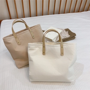 Detail of minimalist tote bags with vertical quilted texture and brown leather handles