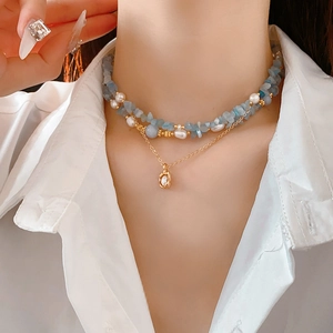 Close-up of double layer necklace with blue stones, pearls and gold pendant on a model