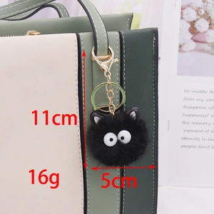 Black faux mink fur pompom keychain charm with large eyes on a green handbag