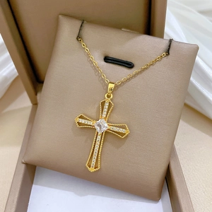 Close-up of golden hollow cross necklace with square crystal in a beige jewelry box