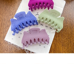 Gros plan de quatre grandes pinces à cheveux mates floquées en violet, bleu et vert