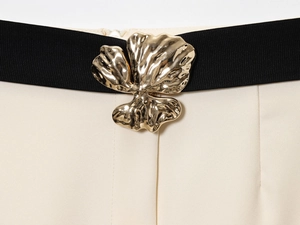 Détail d'une ceinture noire avec boucle fleur dorée sur une jupe blanc cassé