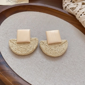 Detail view of woven raffia and wooden square drop earrings on rustic linen background