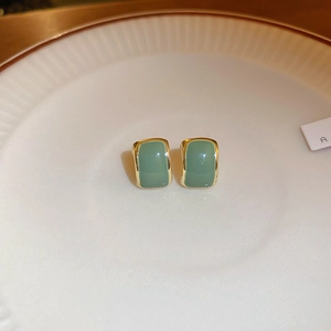 Macro shot of vintage green square stud earrings with gold metal trim on a white plate