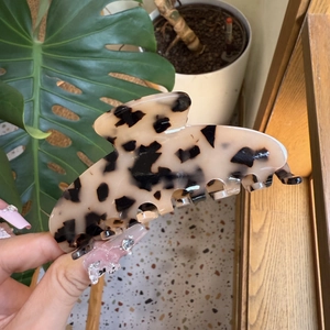 Detail of a large leopard print acetate hair claw clip held by hand for scale