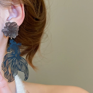 Detailed close-up of resin flower and blue koi fish dangle earrings worn on an ear