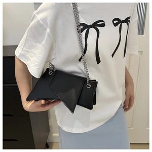 Detail of black asymmetric geometric crossbody bag with silver chain strap on model