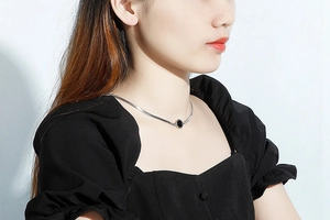 Close-up of gold flat snake chain necklace with circular black shell pendant on model