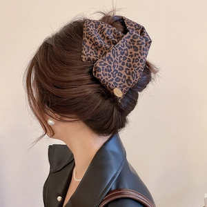 Detail of vintage leopard print hair claw with a gold brand tag on a brown bun hairstyle