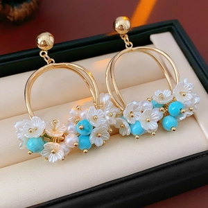 Detailed shot of gold floral earrings with white petals and blue beads in a jewelry box
