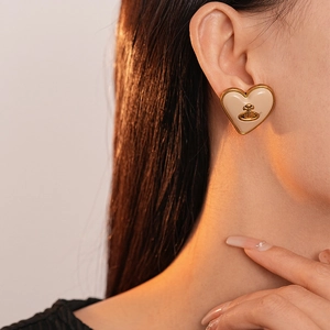 Détail d'une boucle d'oreille cœur avec logo orb doré sur résine beige vintage