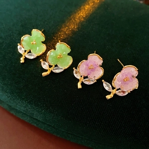 Close-up of gold-plated flower stud earrings with green and purple crystals on velvet