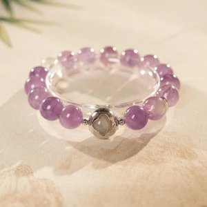 Detail of amethyst beaded bracelet with hollow silver clover bead on textured beige background