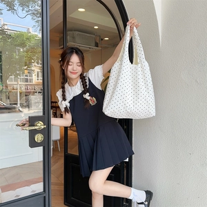 Detail of white polka dot canvas tote bag paired with navy pleated academic style dress