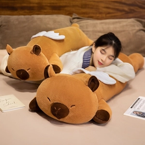 Soft plush capybara body pillow with white wings in a warm bedroom setting