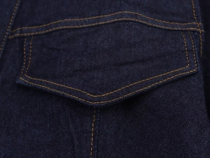 Vista macro di una tasca in denim indaco con cuciture arancioni a contrasto e twill