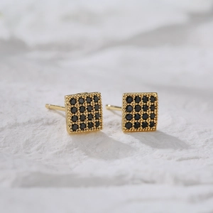 Square gold-plated earrings with micro-set black zircons on a white textured background