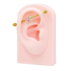 Close-up of golden industrial barbell featuring pink heart gem and golden wing detail