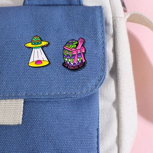 Cute cartoon dinosaur enamel pins set on a blue canvas bag featuring a UFO and eggshell badge