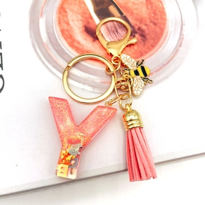 Detail of pink resin letter Y keychain with gold bee pendant and leather tassel