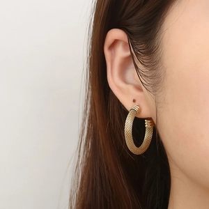 Élégantes créoles en acier inoxydable plaqué or 18K avec texture maille sur un modèle
