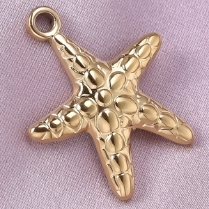 Detailed view of a golden textured starfish pendant on soft purple silk fabric