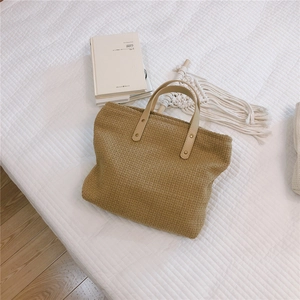 Detail view of woven khaki tote bag with leather handles and gold rivet accents on fabric