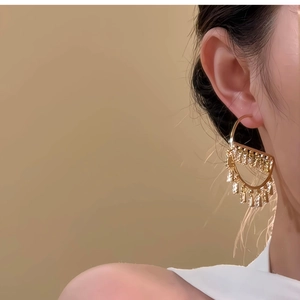 Close-up of elegant gold-plated D-shape hoop earrings with trapezoid zircon pendants on model