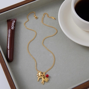 Detailed shot of a gold-plated evil eye necklace with horse and clover charms on felt tray