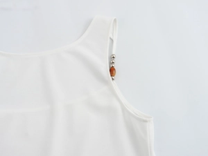 Detail of white camisole top featuring decorative metal and amber beaded shoulder straps