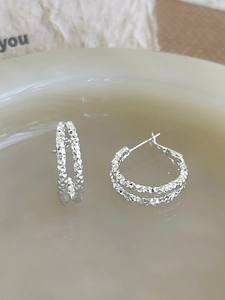 Macro shot of silver geometric double hoops with diamond-cut texture on ceramic plate