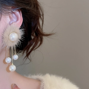 Close-up of elegant long tassel earrings with beige fur balls and pearls on model
