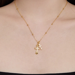 Detail of gold double cross pendant necklace featuring beaded chain and zircon micro-paving
