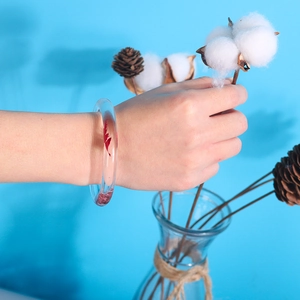 Close-up of a transparent resin bracelet with red leaf inlay on a blue background