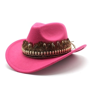 Detail of rose pink felt cowboy hat featuring brown feathers and gold skull charms