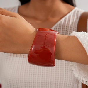 Close-up of wide red resin bangle on a white knitted sleeve highlighting its glossy finish
