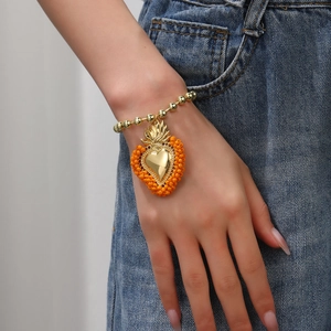 Detail eines Perlenarmbands mit goldenem Herzanhänger und orangefarbenen Mikroperlen