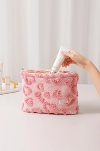 Détail de la trousse de maquillage en peluche rose avec motifs de cœurs embossés