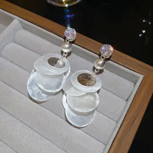 Elegant zircon earrings with layered shell pendants and silver beads on a grey display
