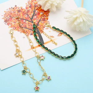 Detail of gold star charm bracelet and green gemstone tennis chain on blue backdrop