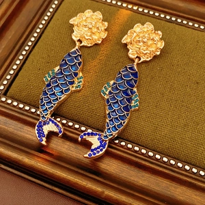 Macro shot of vintage gold flower earrings with a blue koi fish pendant and crystals