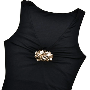 Détail d'une robe noire à col en V avec une élégante broche florale dorée en gros plan