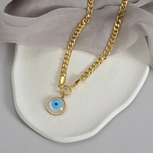 Detail of golden Cuban chain and Evil Eye pendant on stone base with silk backdrop