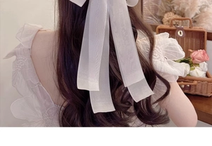Detail view of large white organza bow hair clip worn on long wavy brown hair