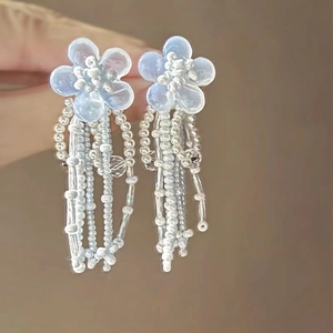 Close-up of light blue flower earrings with beaded tassels and elegant floral design